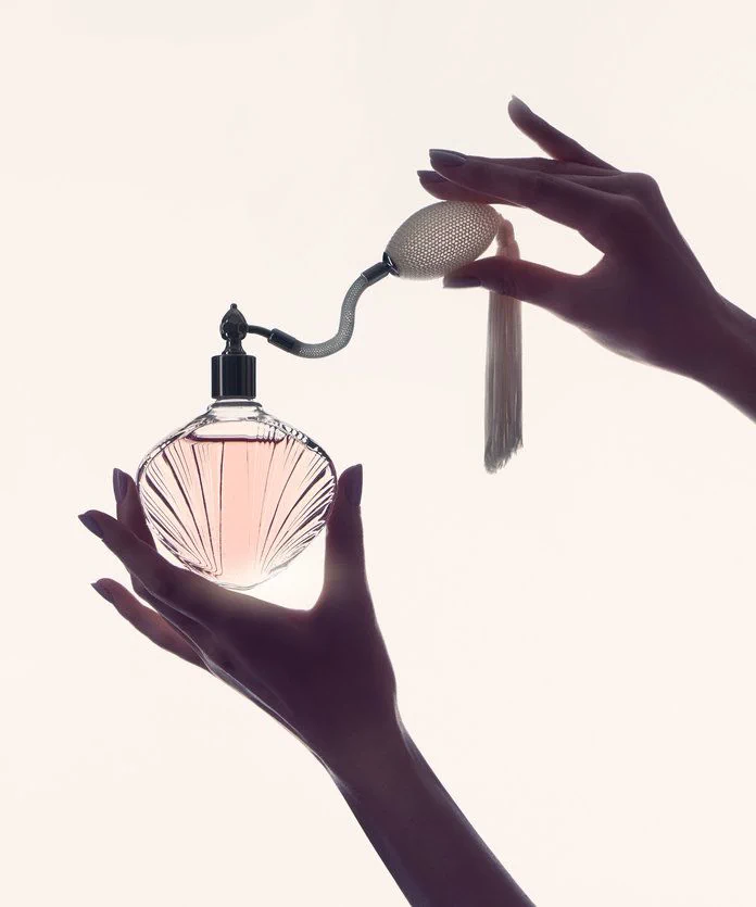 Manos sosteniendo un frasco de perfume vintage con perilla de vaporizador y borla